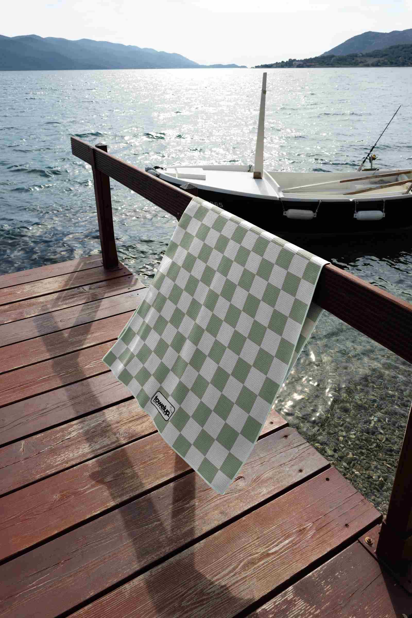 Sage Escape gingham sage sand free beach towel – lifestyle photo showing towel hanging from rail beside ocean