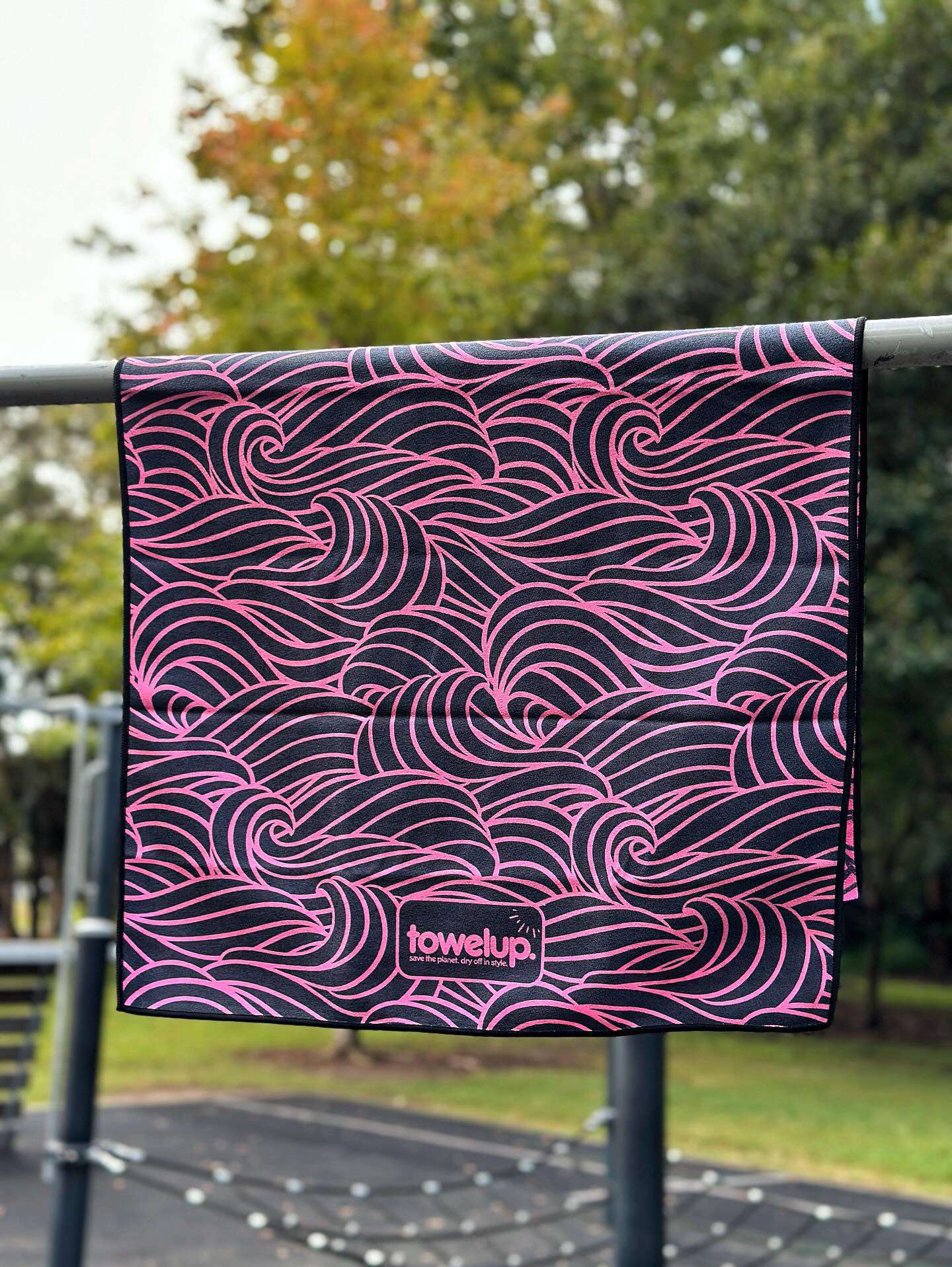 Various gym towels from the brand 'towelup.' hanging up in a park outside. Backdrop of nature and trees.